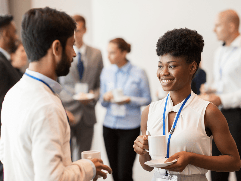 Two professionals engaging in conversation while holding coffee cups at a networking event.